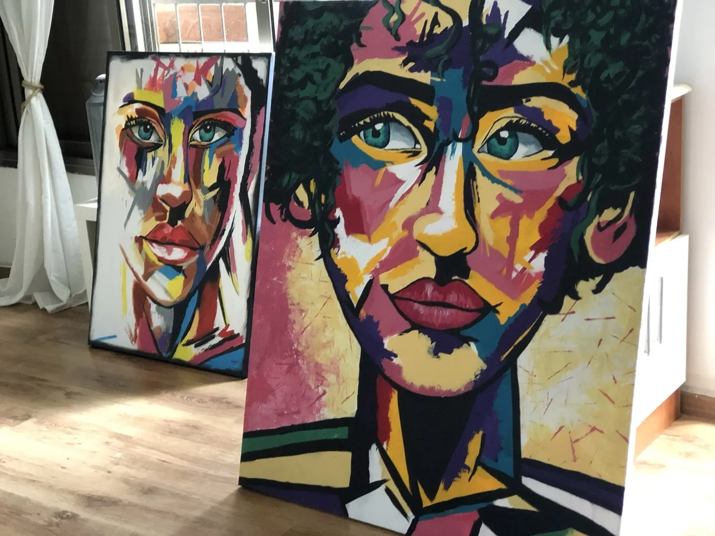 Two acrylic portrait canvases leaning against a wall